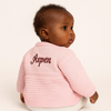 Baby wearing a pink knitted cardigan with 'Aspen' embroidered on the back against a white background