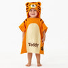 Child wearing an orange tiger-themed poncho with 'Teddy' printed on it against a white background