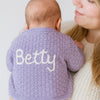 Baby wearing a purple cardigan with 'Betty' embroidered on the back, held by a person.