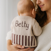 Baby wearing a knitted sweater with 'Betty' on the back, held by a person.