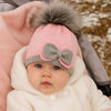 Baby wearing a pink and gray knit hat with a bow, sitting in a stroller.