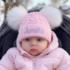 Baby in pink winter outfit with 'Amelia' on hat, sitting in a stroller.