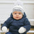 Baby wearing a blue snowsuit and white hat with 'Freddie' on it, sitting outdoors.