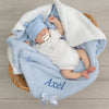 Newborn baby wrapped in a blue blanket with 'Axel' embroidered, wearing a matching blue hat and white outfit, in a wicker basket.