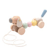 The New Bambino Draft Bambino Wooden Pull Along Dog is a delightful toddler toy. Its body is composed of smooth, pastel-colored beads with a blue handle at the back. A string attached to its front allows it to be pulled along as it moves on wheels.